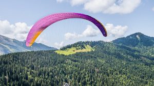 Experience an adventurous paragliding flight over lush alpine landscapes under a vibrant sky.
